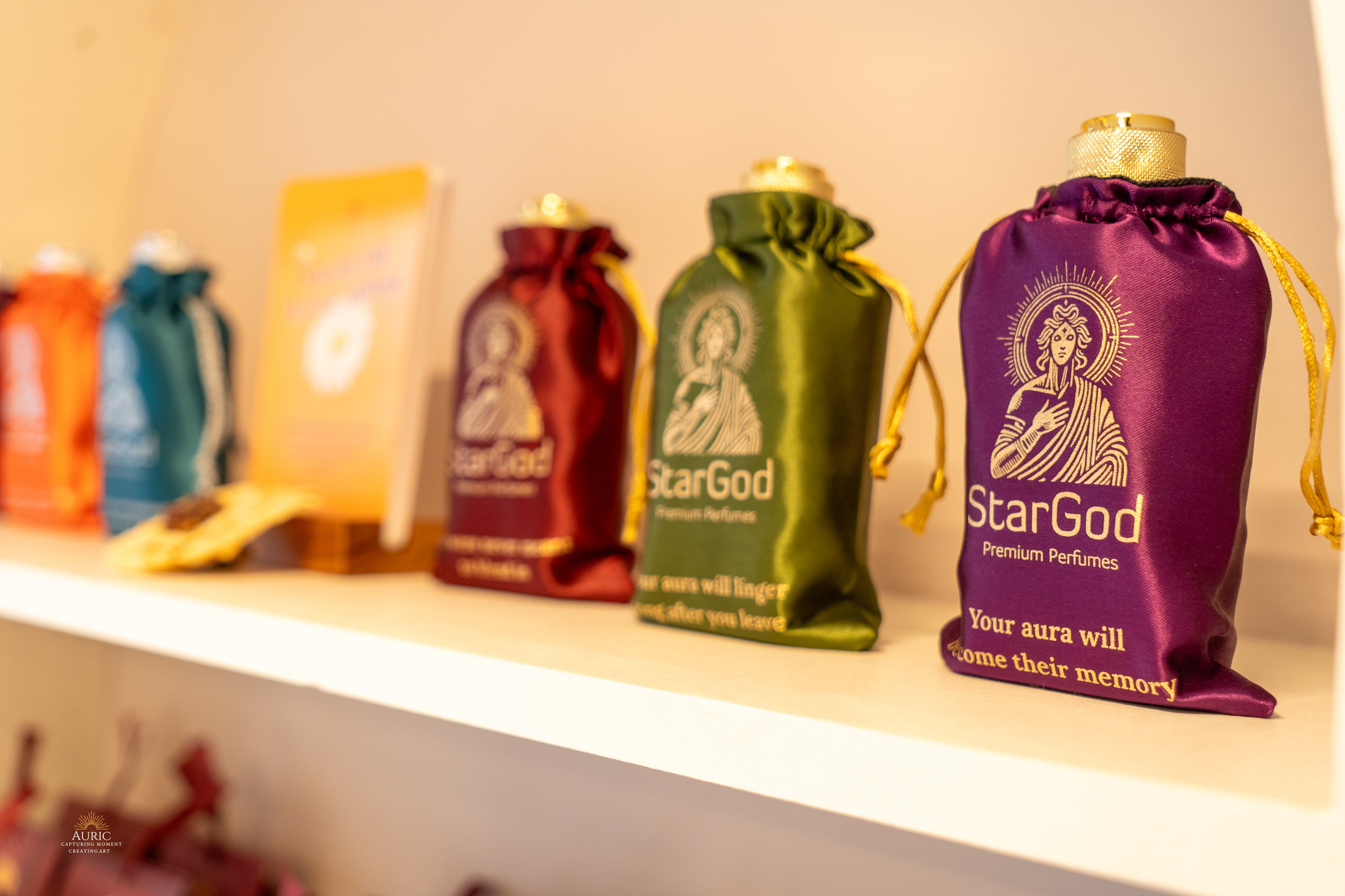 Burgundy, olive-green, and royal-purple satin drawstring pouches on a boutique shelf, each printed with a different line in cream.
